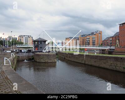 Blick auf die Schleusentore vor dem clarence Dock in leeds mit den Leuten auf der Insel neben der Ritterbrücke und dem Stadtapartment Stockfoto