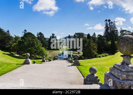 Ein breiter Fußweg führt zum See mit Brunnen, umgeben von grünen Bäumen, Sugerloaf-Berg im Hintergrund, Powerscourt Gardens, Wicklow, Irland Stockfoto