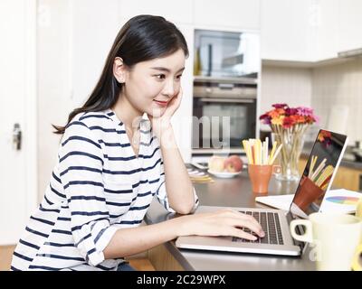 Junge asiatische Geschäftsfrau arbeiten von zu Hause sitzen an der Küchentheke mit Laptop-Computer Stockfoto