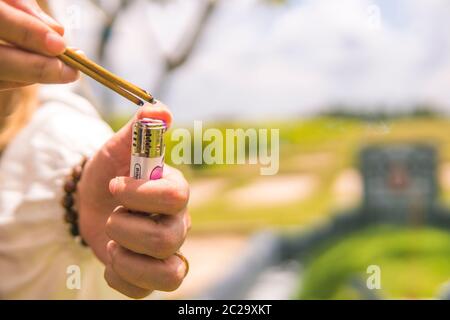 Nahaufnahme der Hand einer Frau, die Weihrauch verbrennt. Der Hintergrund ist ein unidentifiziertes Gräber, verschwommen Stockfoto