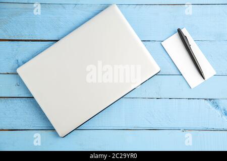 Grau Laptop und Notizbuch aus Papier mit schwarzer Tinte auf Blau Holz- Hintergrund. Der Blick von oben Stockfoto