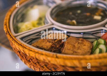 Reisschüssel mit Rattan, innen ist traditionelles vietnamesisches Mittagessen, Reis, Suppe, salziges Essen. Die Szene ist sparsam und friedlich. Essen und Trinken Konzept. Stockfoto