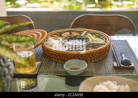 Reisschüssel mit Rattan, innen ist traditionelles vietnamesisches Mittagessen, Reis, Suppe, salziges Essen. Die Szene ist sparsam und friedlich. Essen und Trinken Konzept. Stockfoto