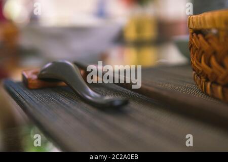 Nahaufnahme von Holzlöffel und Essstäbchen neben einem Rattan-Reis-Schüssel, innen ist ein traditionelles vietnamesisches Mittagessen, Reis, Suppe, salziges Essen. Stockfoto