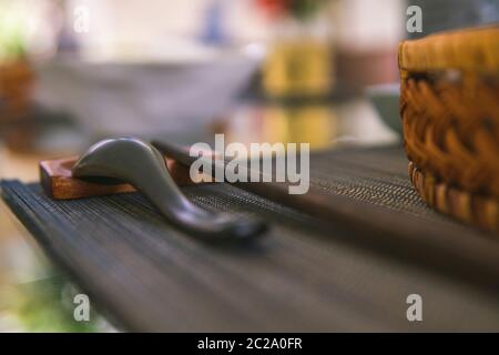 Nahaufnahme von Holzlöffel und Essstäbchen neben einem Rattan-Reis-Schüssel, innen ist ein traditionelles vietnamesisches Mittagessen, Reis, Suppe, salziges Essen. Stockfoto