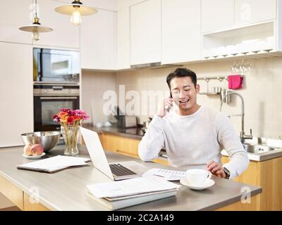 Junge asiatische Geschäftsmann sitzen Küche Zähler zu Hause im Gespräch auf Handy lachen Stockfoto