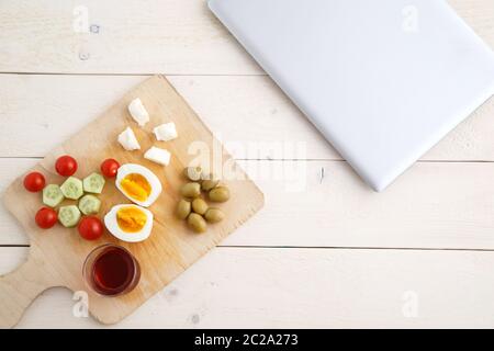 Tee und türkisches, mediterranes Frühstück auf einem hellen Holztablett auf weißem, natürlichem Hintergrund. Und ein geschlossener Laptop vor der St. Stockfoto