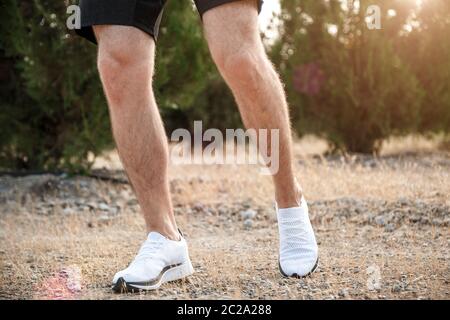 Die Füße der Männer in weißen Turnschuhen über unebenes Gelände laufen. Querfeldein laufen mit Fokus auf die Beine Runner. Stockfoto