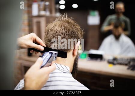 Mann, der einen Haarschnitt mit einem Haarschneider im Friseursalon hat Stockfoto