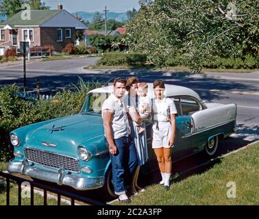 Eine Familie posiert neben ihrem zweifarbigen Chevrolet Bel Air in ihrer Vorstadteinfahrt, USA, 1961 geparkt. Die Gruppe umfasst das Baby des jungen Paares. Dieser Chevy, ein 2-türiger Hardtop, wurde von 1953 bis 1957 hergestellt.