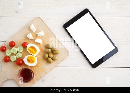 Tablette, Tee und türkisches, mediterranes Frühstück vor dem Start des Arbeitstages oder während der Arbeit auf einem hellen Holztablett auf einem Stockfoto