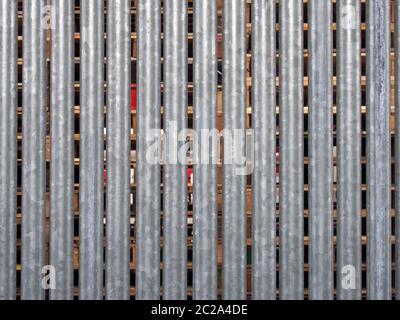 Vertikaler verzinkter Stahlzaun mit Holzpaletten im Außenlager, sichtbar zwischen den Lücken Stockfoto