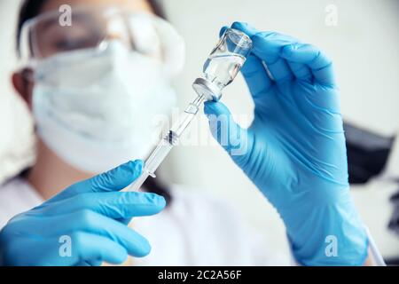 Wissenschaftler zieht Medizin in die Spritze. Wissenschaftlerin in Schutzmaske, Brille und Handschuhe zieht Medizin in die Spritze. Stockfoto
