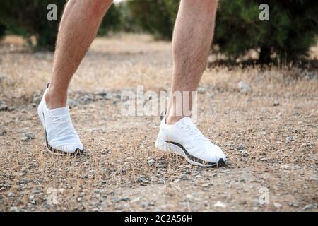 Die Füße der Männer in weißen Turnschuhen über unebenes Gelände laufen. Querfeldein laufen mit Fokus auf die Beine Runner. Stockfoto