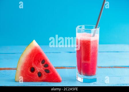 Ein Stück Wassermelone und Smoothie Wassermelonen, frisch gepressten Saft in ein transparentes Glas auf einem blauen Hintergrund aus Holz Stockfoto