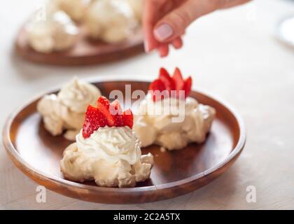 Der Prozess der Herstellung von Pavlova Dessert, die Dekoration der Meringue mit Erdbeeren Stockfoto