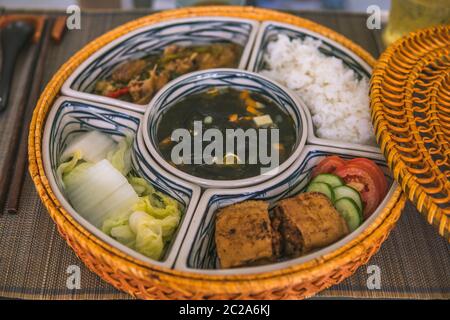 Reisschüssel mit Rattan, innen ist traditionelles vietnamesisches Mittagessen, Reis, Suppe, salziges Essen. Die Szene ist sparsam und friedlich. Essen und Trinken Konzept. Stockfoto