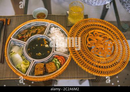 Reisschüssel mit Rattan, innen ist traditionelles vietnamesisches Mittagessen, Reis, Suppe, salziges Essen. Die Szene ist sparsam und friedlich. Essen und Trinken Konzept. Stockfoto