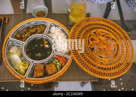 Reisschüssel mit Rattan, innen ist traditionelles vietnamesisches Mittagessen, Reis, Suppe, salziges Essen. Die Szene ist sparsam und friedlich. Essen und Trinken Konzept. Stockfoto