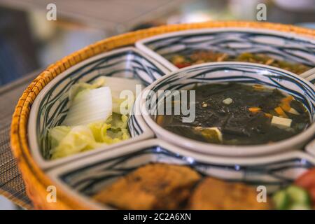 Reisschüssel mit Rattan, innen ist traditionelles vietnamesisches Mittagessen, Reis, Suppe, salziges Essen. Die Szene ist sparsam und friedlich. Essen und Trinken Konzept. Stockfoto