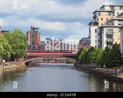 Ein Blick auf den Fluss aire in leeds mit Apartments und Gebäuden am Wasser mit einer Crown Point Brücke über das Wasser Stockfoto