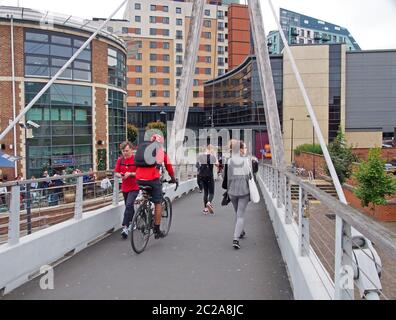 Menschen wandern und radeln über die Millennium Bridge in leeds mit Gebäuden und Bars am Wasser Stockfoto