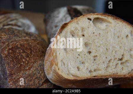 Ein frischer knuspriger Laib hausgemachtes Brot. Hausgemachte rustikale sauer. Braunes Brot. Verschiedene Arten von Broten. Brotscheiben. Atmosphärenbild einer Küche im Landhausstil. Stockfoto