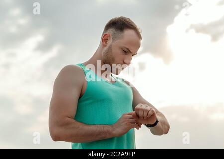 Portrait der kaukasischen Kerl in Azure t-shirt Fitness tracker Lesungen vor oder nach dem Joggen. Stockfoto