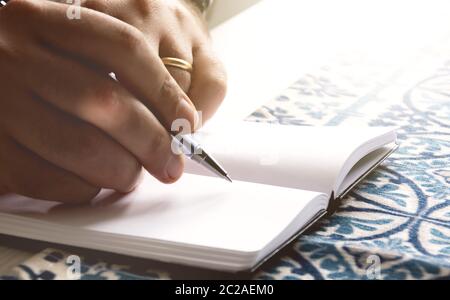 Männliche Hände halten einen Kugelschreiber, um auf die leeren Seiten eines offenen Notizbuchs zu schreiben.