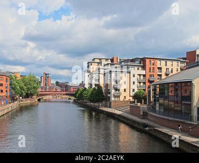 Ein Blick auf den Fluss aire in leeds mit Wohnhäusern rund um die Crown Point Brücke und Menschen, die entlang der Uferpromenade spazieren Stockfoto