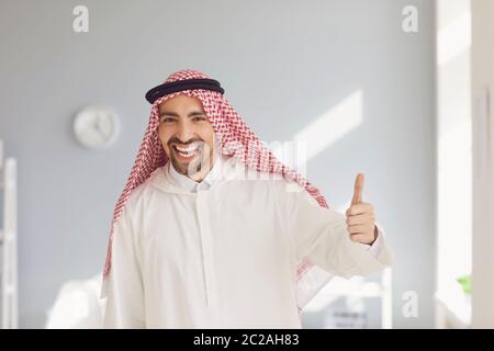 Ein glücklicher arabischer Mann hob seinen Daumen in einem weißen Büro auf Stockfoto