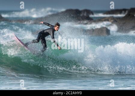 Spektakuläre Surfaktion, während ein junger männlicher Surfer eine Welle in Fistral in Newquay in Cornwall reitet. Stockfoto