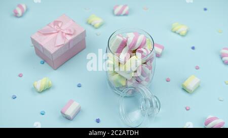 Köstliche bunte Marshmallows im Glas und kleine Herzen auf einem blauen Tisch Stockfoto