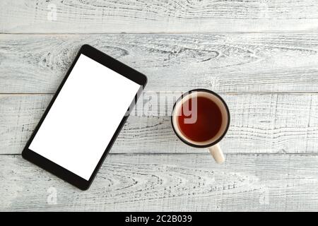 Elektronische Tablette mit einer Tasse Tee oder Kaffee auf einem Vintage shabby weiß Holz- Hintergrund. Die Aussicht von oben. Flach Stockfoto