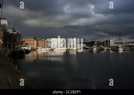 Marina und die umliegenden Gebäude in Ipswich, Suffolk, Vereinigtes Königreich mit sehr dunklen Gewitterwolken und Sonnenlicht beleuchtet die Boote und Bu Stockfoto