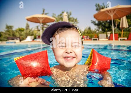 Ein kleiner Junge lernt in den Pool im Sommer zum Schwimmen mit der Unterstützung von den Händen seines Vaters