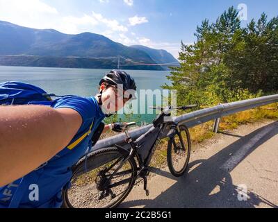 Thema des Mountainbiking in Skandinavien. Menschlicher Tourist in Helm und Sportbekleidung auf Fahrrad in Norwegen auf Hardanger Brücke suspens Stockfoto