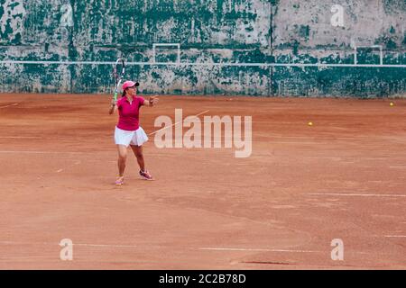 Tennis Player. Athlet Frau Tennis spielen, ein dienen, in rosa T-Shirt, eine Kappe und weißen Rock gekleidet. Seitenansicht, auf dem Gericht. Stockfoto