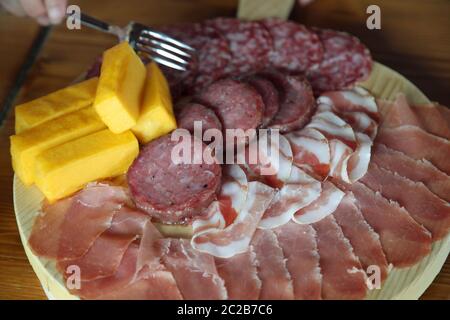 Gabel, die gemischte Aufschnitte aus dem Holzschneidebrett im italienischen Bauernhaus nimmt Stockfoto