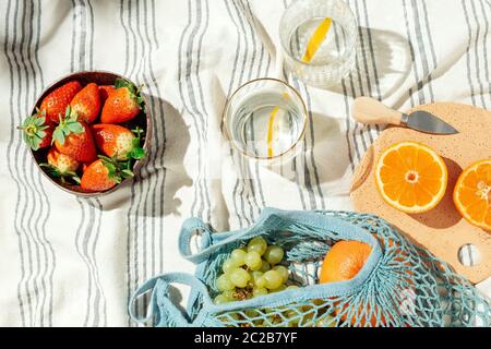 Feminine Sommer Picknick Flatlay, Früchte, String Öko-Bag und Zitronenwasser auf gestreiften Baumwolldecke Stockfoto