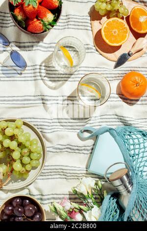 Feminine Sommer Picknick-Flatlay, Früchte, Beeren und Zitronenwasser auf gestreifter Baumwolldecke Stockfoto