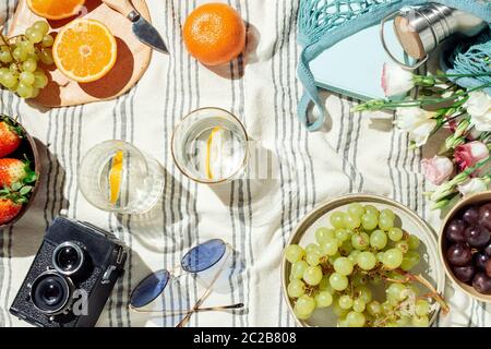 Feminine Sommer Picknick-Flatlay, Früchte, Beeren und Zitronenwasser auf gestreifter Baumwolldecke Stockfoto