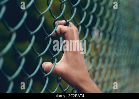 Junger Mann Hand hält am Kettenglied Zaun für Freiheit, Tag der Menschenrechte, Immigrant Konzept. Stockfoto