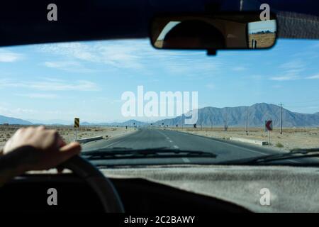 Inspirierendes Roadtrip-Bild mit Hand am Rad - Iraner fährt auf Wüstenstraße, Berge im Hintergrund in der Nähe der Provinz Yazd im Iran Stockfoto