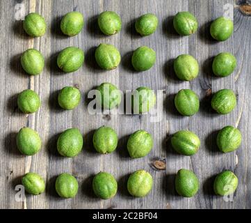 Junge grüne Früchte der Walnüsse liegen in den Zeilen auf einem grauen Hintergrund aus Holz. Stockfoto