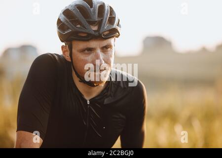 Portrait des sportlichen Mannes in schwarzem Helm und Radbekleidung nass wegen des harten Trainings und Reiten lange Strecke. Professioneller Fahrradfahrer relaxin Stockfoto