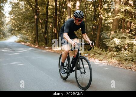 Aktiver bärtiger Mann in Sportkleidung und schwarzem Helm Fahrrad mit schöner Natur rund reiten. Reifer Radfahrer in Spiegelbrille tun Favorit Stockfoto