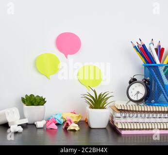 Stapel von Notebooks, Buntstifte in einem blauen Glas, grüne Pflanzen in Töpfen und kabellose Kopfhörer auf einem schwarzen Holztisch, Platz für ein Designer und fr Stockfoto