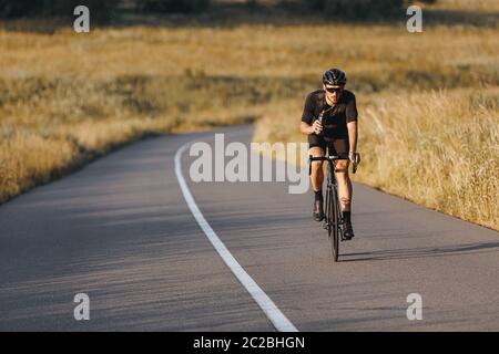 Reife Sportler in activewear, Schutzhelm und Sonnenbrille Reiten Fahrrad und halten Flasche mit Wasser. Professioneller Radfahrer macht Lieblings-Hobby Stockfoto