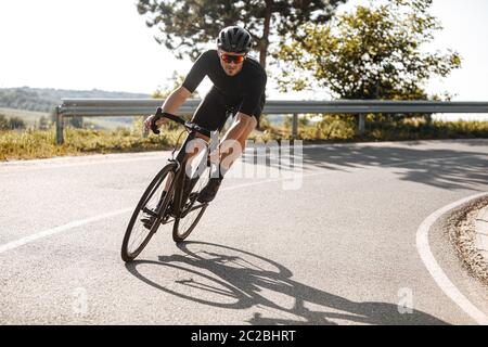 Bärtiger Radfahrer in Sportkleidung, Schutzhelm und Spiegelbrille Reiten schwarzen Fahrrad inmitten der Natur im Sommer. Reifer Mann PR Stockfoto